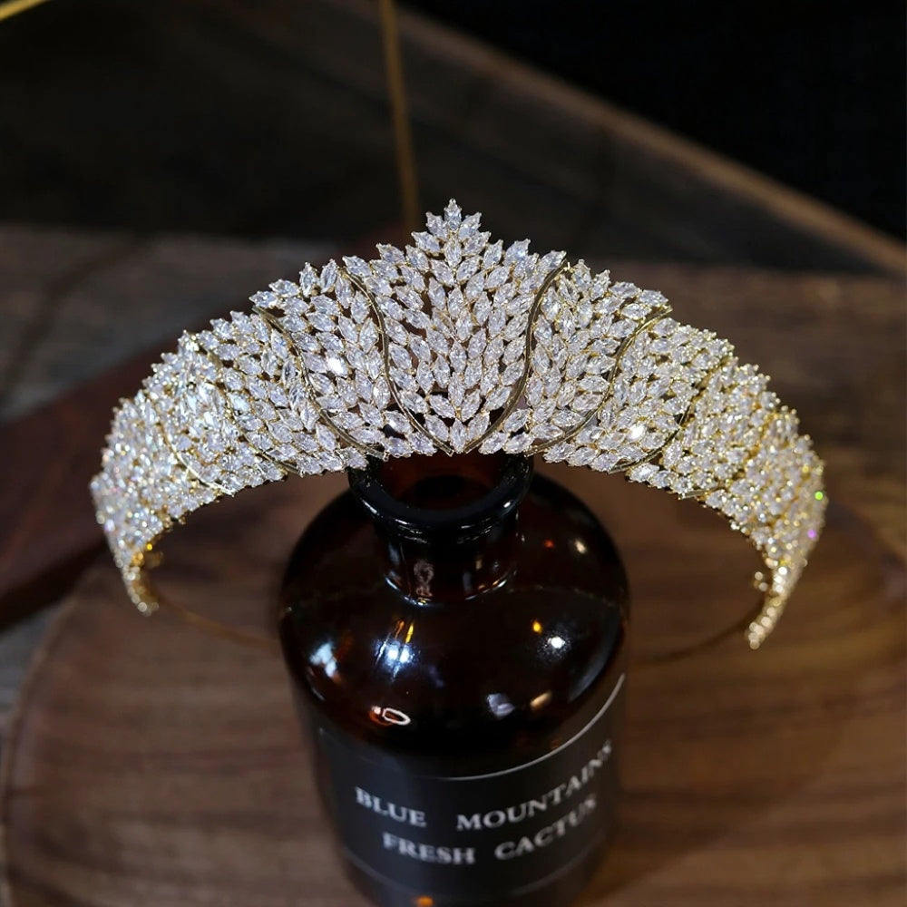 Front profile view of a luxury gold crystal bridal tiara crown meticulously balanced on a dark glass display bottle.
