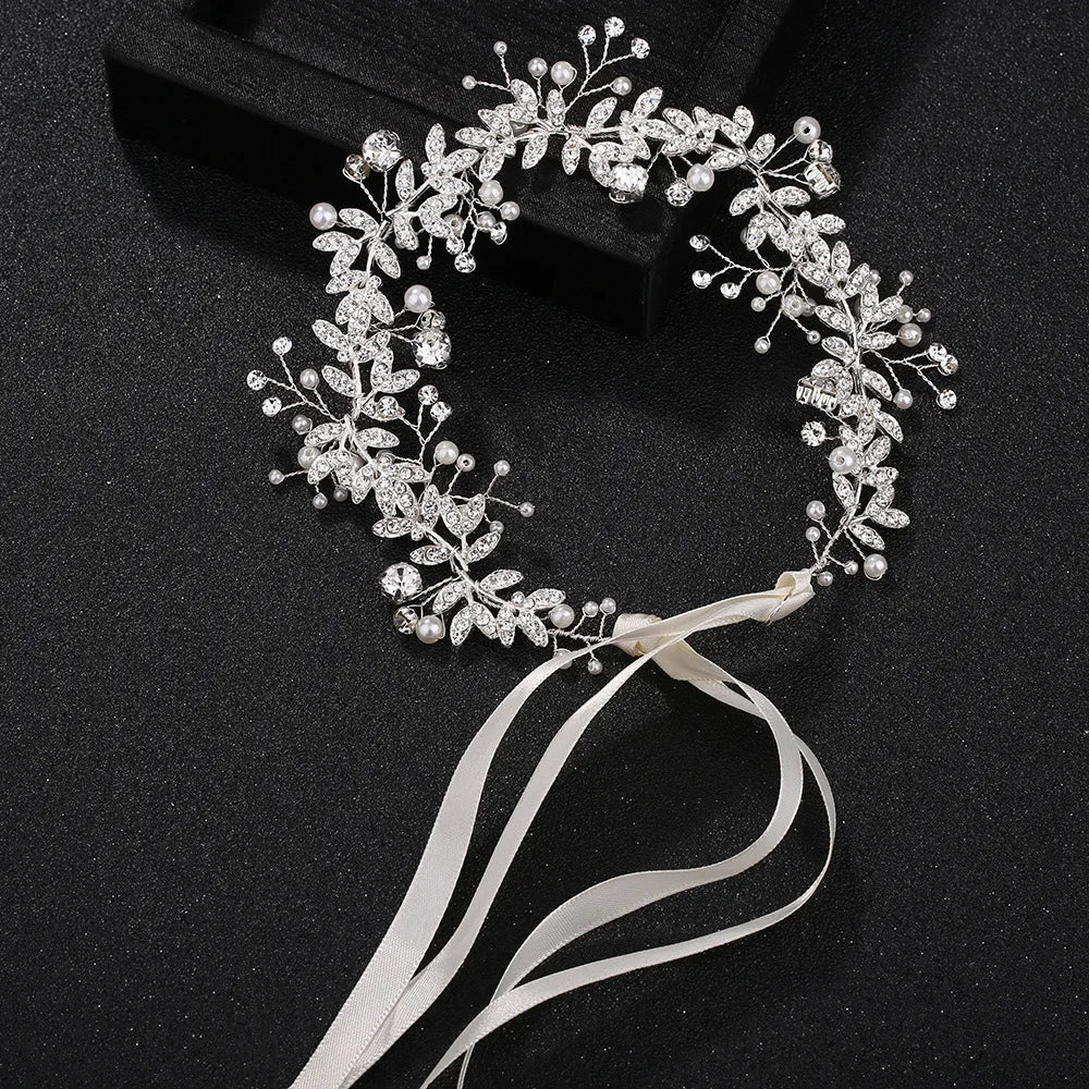 A silver-toned crystal and pearl bridal headband with delicate white ribbons on a black display surface.