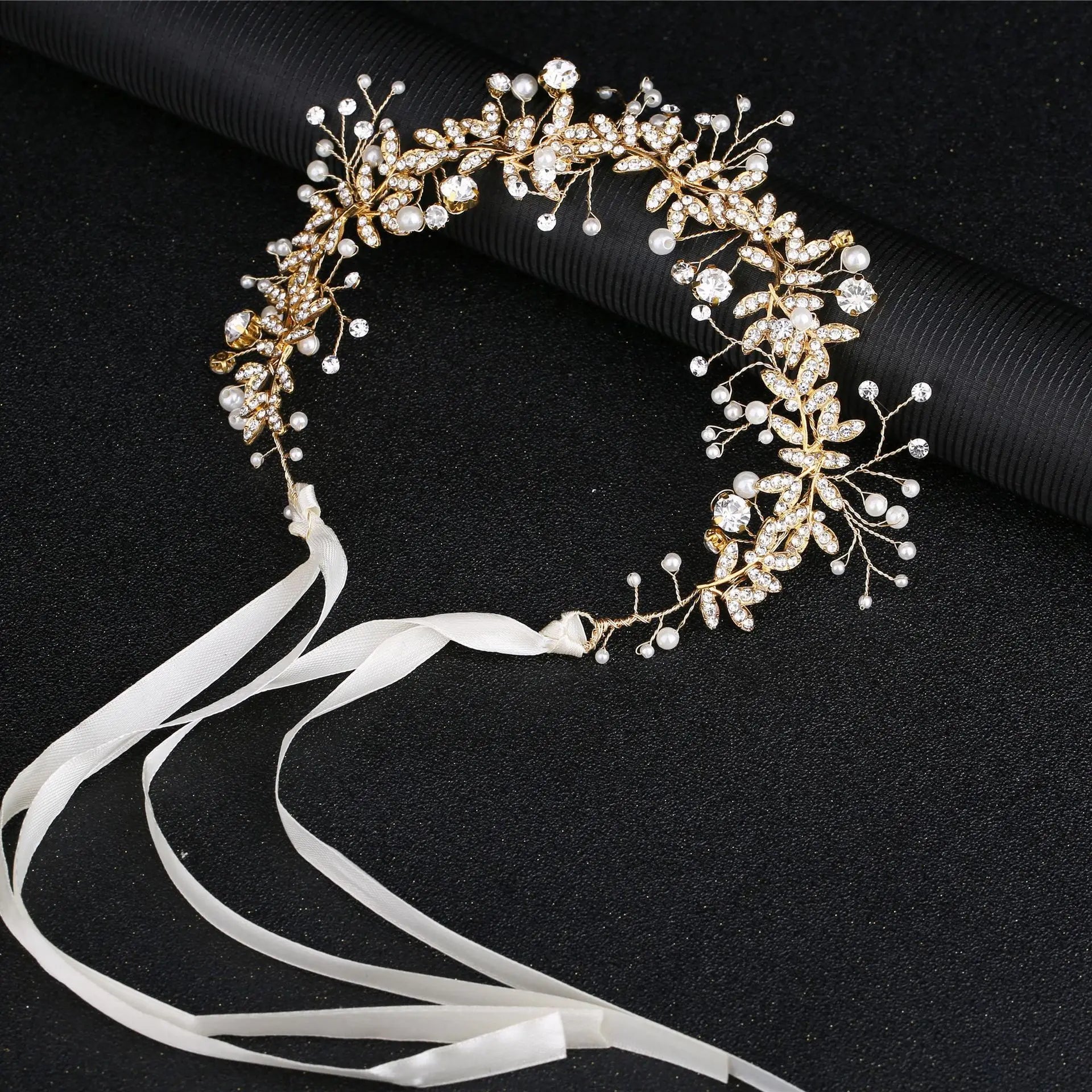 Elegant gold wedding headband featuring crystal flowers, pearls, and long white ribbons on a black background.