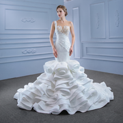 Full-length front view of a model wearing a luxury crystal mermaid wedding dress featuring an intricate pearl lace bodice and a dramatic, voluminous ruffled satin skirt.
