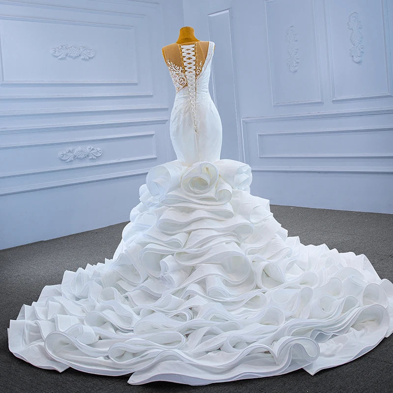 Rear view of a luxury mermaid bridal gown on a mannequin, showcasing the elegant lace-up corset back, sheer lace embroidery, and wide ruffled train.