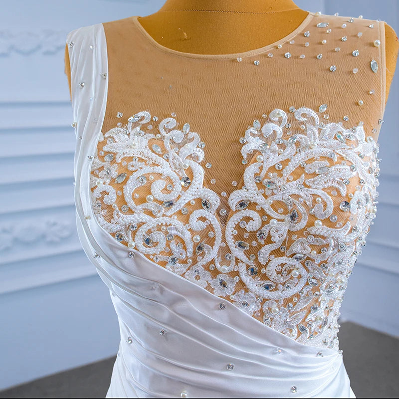 Close-up of a bridal gown bodice featuring sheer illusion netting adorned with delicate lace appliqués, shimmering crystals, and hand-sewn pearls.