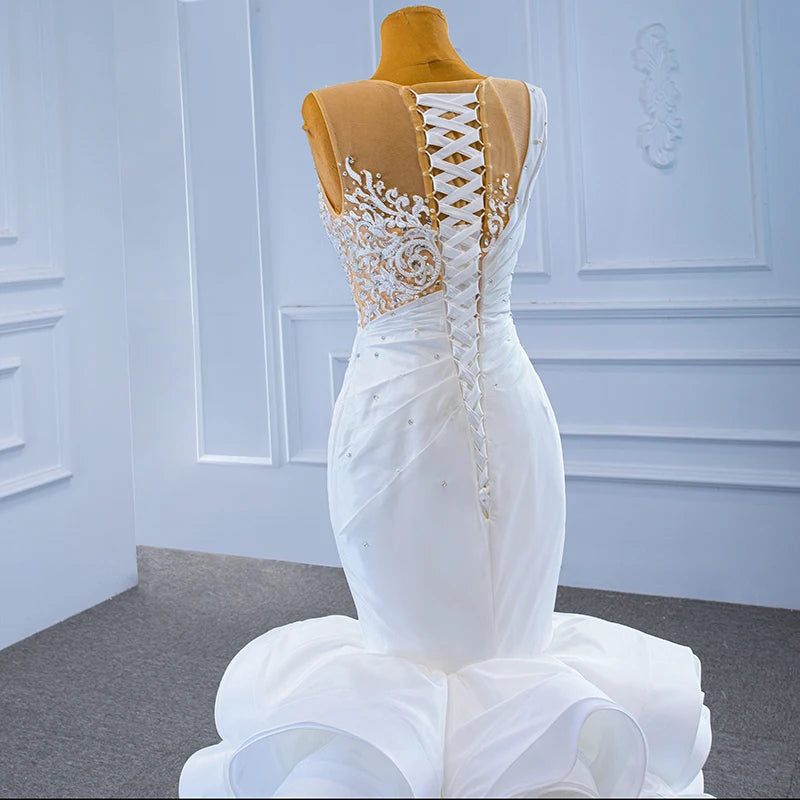 Rear detail of a bridal dress on a mannequin featuring a traditional white lace-up corset closure and intricate floral lace embroidery with pearl accents on a sheer back.