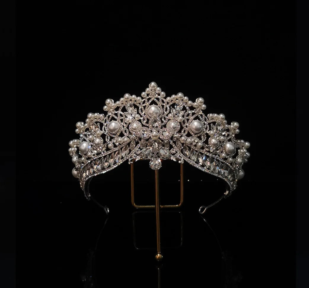 Front view of a luxury crystal and pearl bridal crown, perfectly balanced on a metal display stand.