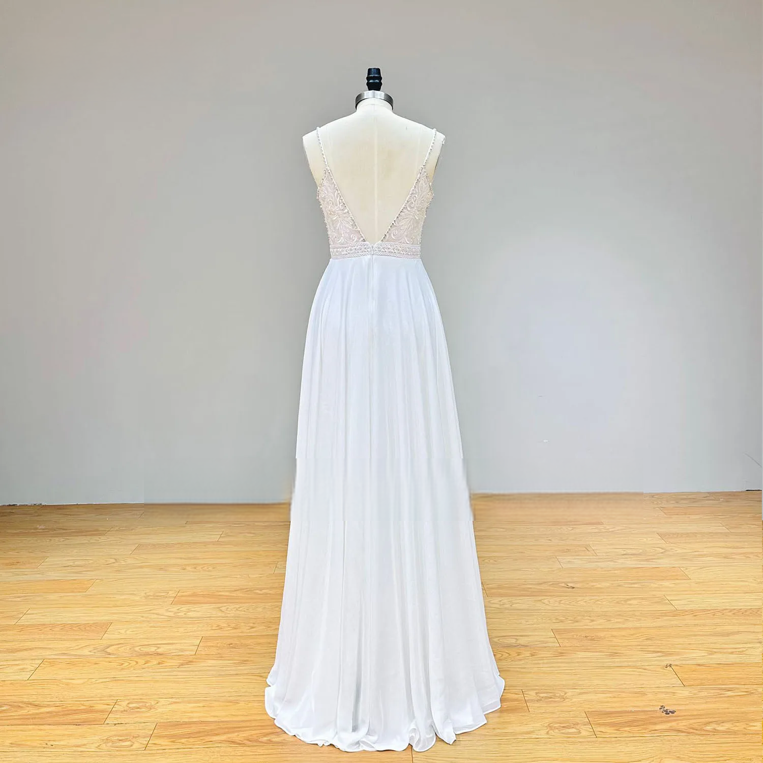 Full-length rear view of a backless chiffon wedding dress on a mannequin, emphasizing the flowing pleated skirt and delicate lace V-back detailing.