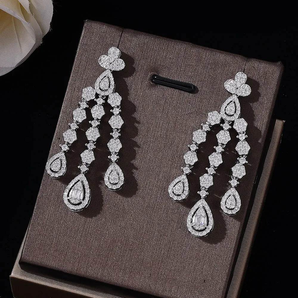 Close-up view of elegant cubic zirconia chandelier bridal earrings showcasing an intricate multi-tier teardrop fringe pattern on a textured brown display mount.