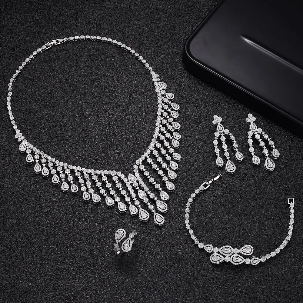 Flat lay product photograph of the luxury silver 4-piece cubic zirconia bridal jewelry collection arranged on a textured black background.