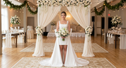 Elegant satin short wedding dress featured in an indoor ceremony setting with a floral archway, showcasing a classic square collar neckline and a dramatic detachable overskirt train
