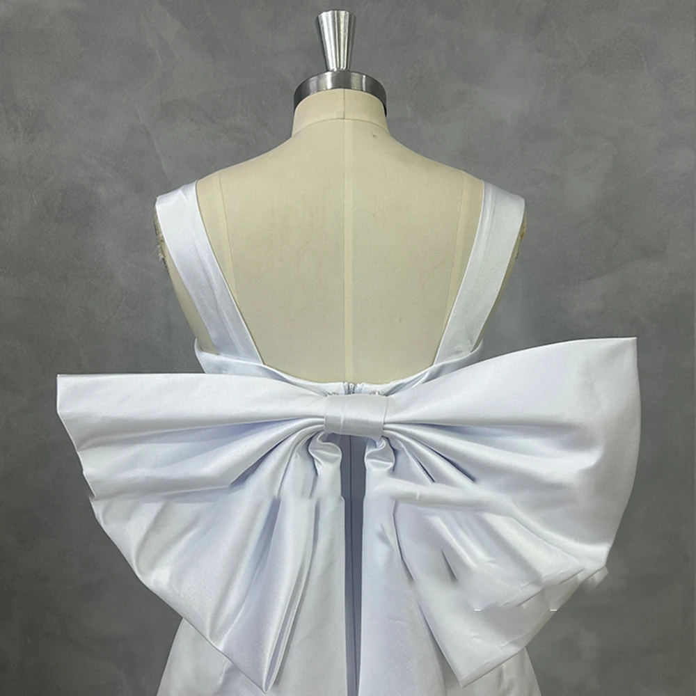 Studio close-up of a low-cut backless satin bridal gown on a mannequin, emphasizing the structural design of an oversized detachable back bow.