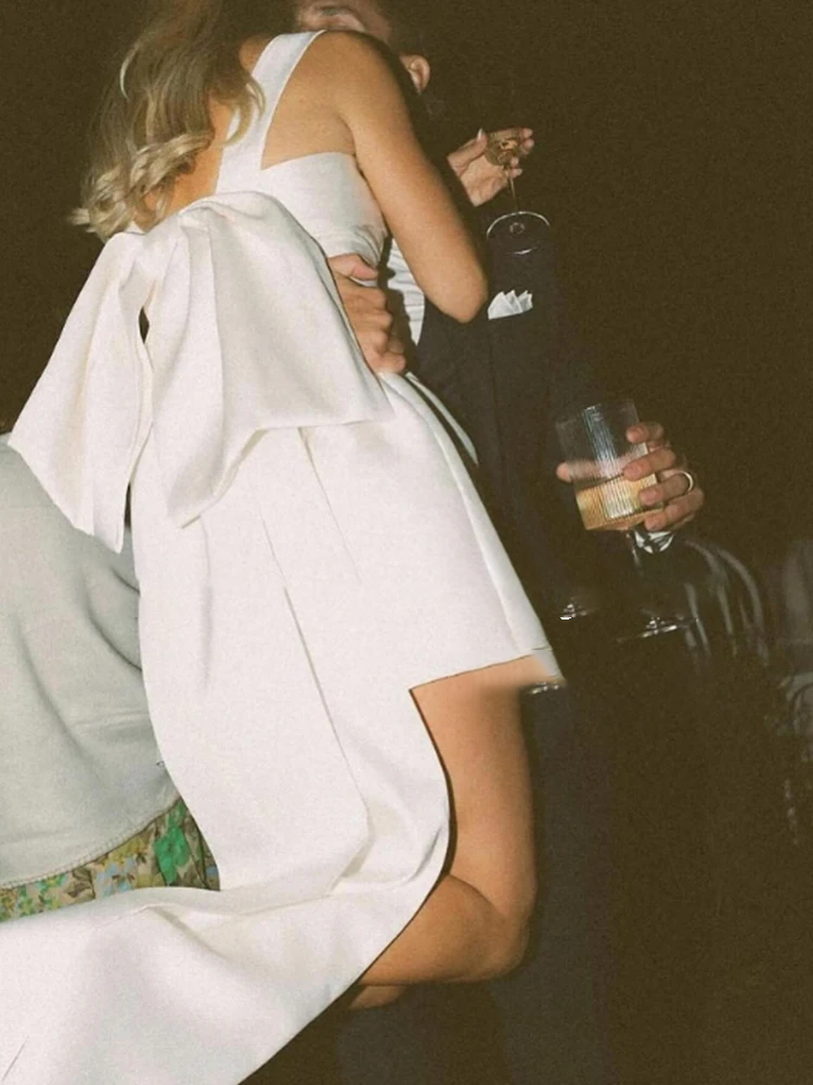 Close-up rear profile of a sexy backless satin bridal mini dress highlighting a deep low open back accented with a massive structural statement bow.