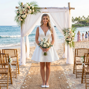 Elegant sleeveless satin short wedding dress featured in a beach elopement under a floral archway, showcasing a plunging V-neckline with illusion mesh and a flared A-line mini skirt.