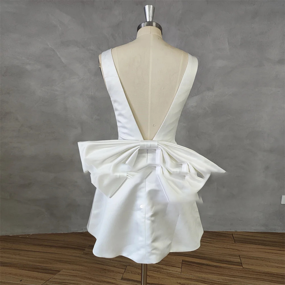 Rear view of a backless short satin wedding gown on a mannequin, showcasing a deep low-V open back design anchored by a large structured oversized bow.