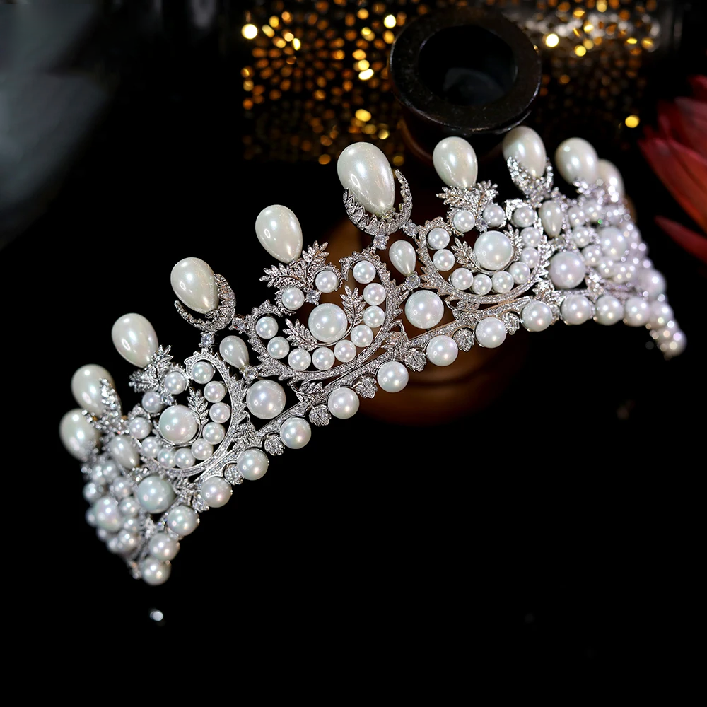 Close-up high-angle view of a luxury bridal crown, showcasing the detailed silver filigree arches, multi-sized pearls, and bright clear crystals.