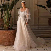 Full-length front view of a bride wearing a romantic tulle wedding dress with a sweetheart neckline, a heavily beaded lace applique bodice, and voluminous detachable sheer long puff sleeves.