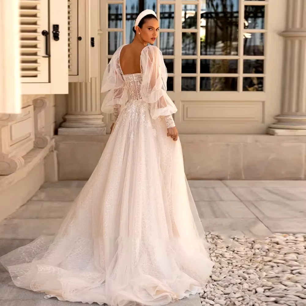 Back view of the glitter tulle bridal gown showcasing the low square back design, intricate corset applique work, and a sweeping chapel-length train paired with statement sheer puff sleeves.