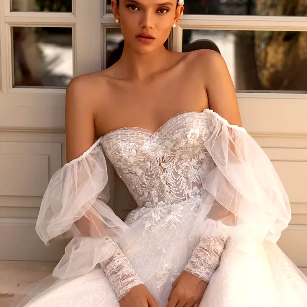 Mid-length close-up portrait highlighting the sheer floral beaded applique bodice with the detachable tulle long sleeves styled in an elegant off-the-shoulder look.