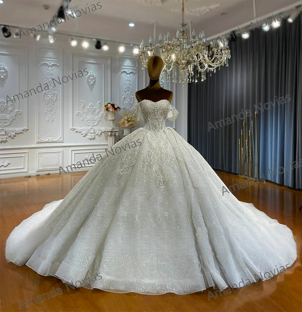 Front-facing view of a regal bridal ball gown on a mannequin, emphasizing the uniform sparkle of the sequined fabric and the high-fashion beaded bodice under a crystal chandelier.