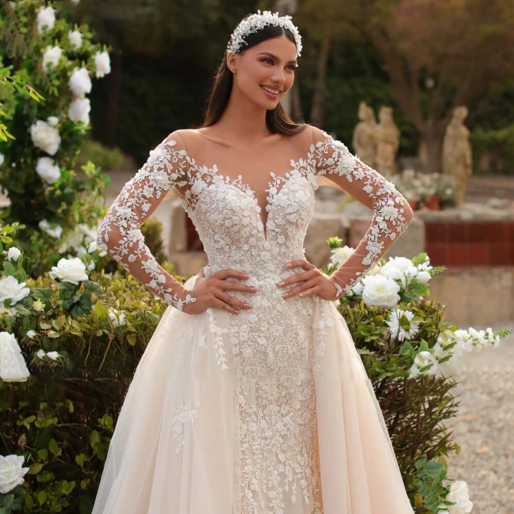 A close-up shot of a bride wearing a white mermaid lace wedding dress with a scoop neck, delicate beaded details, and long sheer sleeves.