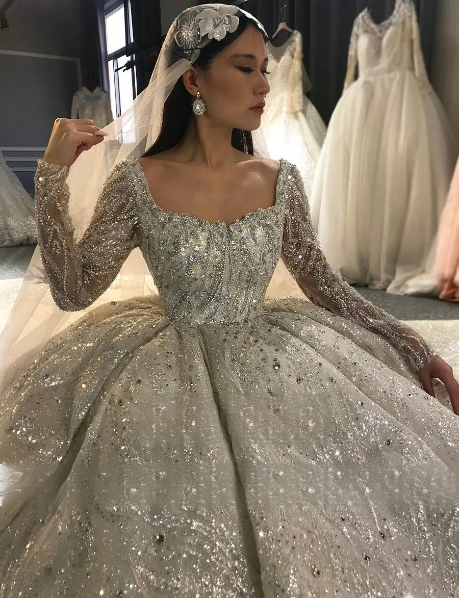 Close-up of the intricate crystal beadwork and silver sequins on the long sleeves and bodice of a royal-style luxury bridal gown.

