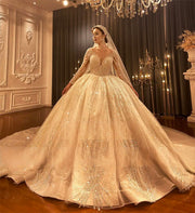 Full-length front view of a Dubai style royal train ball gown wedding dress featuring shimmering gold-tone beadwork and long sheer sleeves in a luxury bridal showroom.