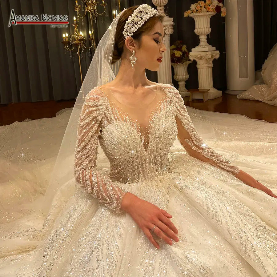 Close-up of a heavily beaded luxury bridal gown bodice with long illusion sleeves and a plunging V-neckline, styled with a pearl headband and cathedral veil.