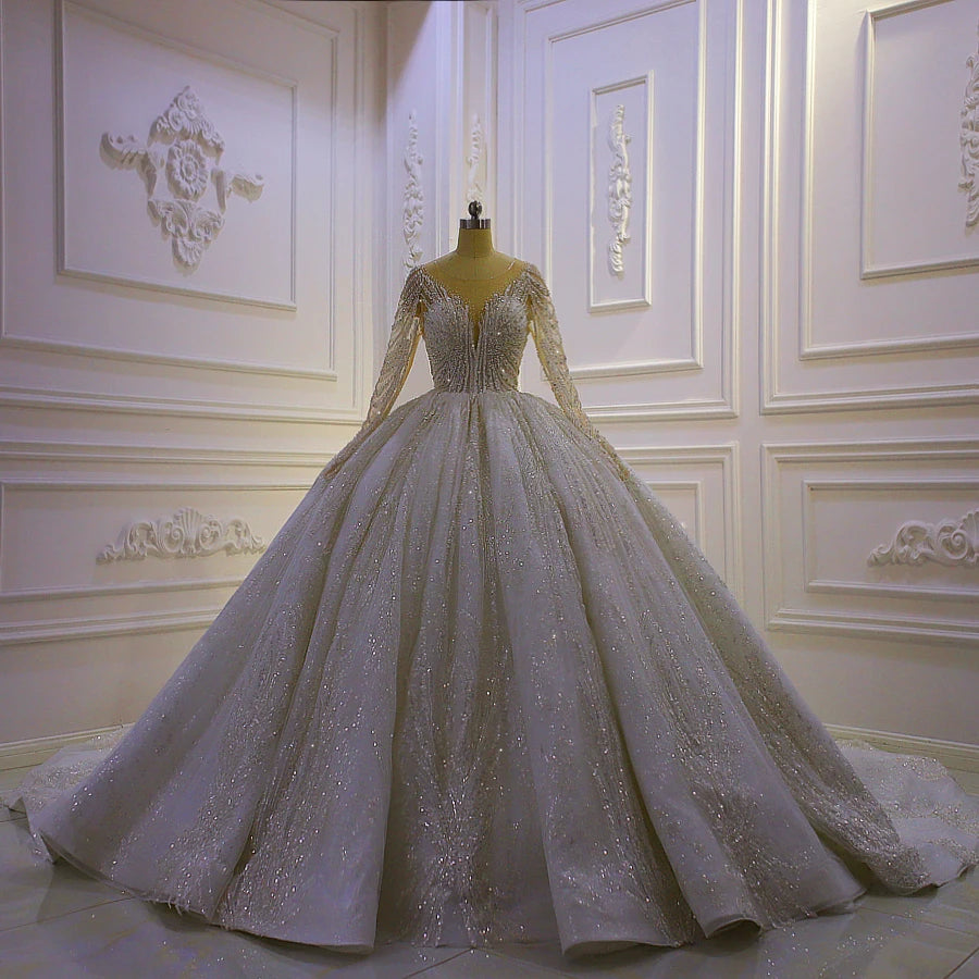 High-fashion display of a luxury long-sleeve ball gown bridal dress on a mannequin, highlighting the intricate silver crystal embroidery and voluminous skirt.
