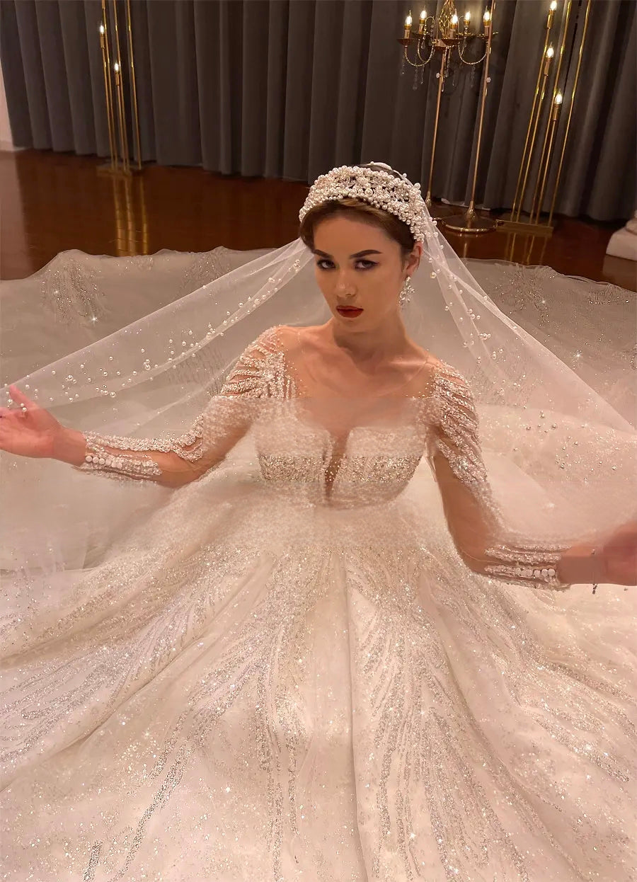 High-angle shot of a bride in a luxury beaded long-sleeve wedding gown, showcasing the intricate glitter branch patterns and a pearl-encrusted bridal veil.