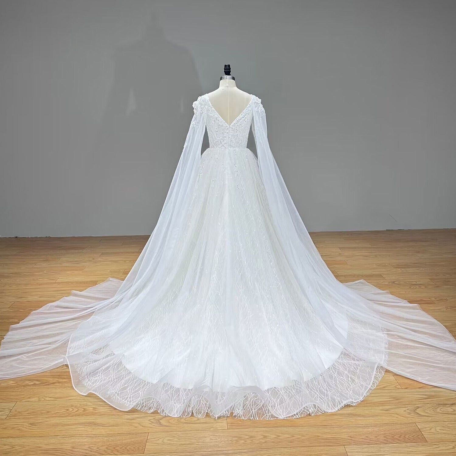 Full back view of an elegant wedding dress showing a V-back zipper closure, shoulder flower accents, and a sweeping train.