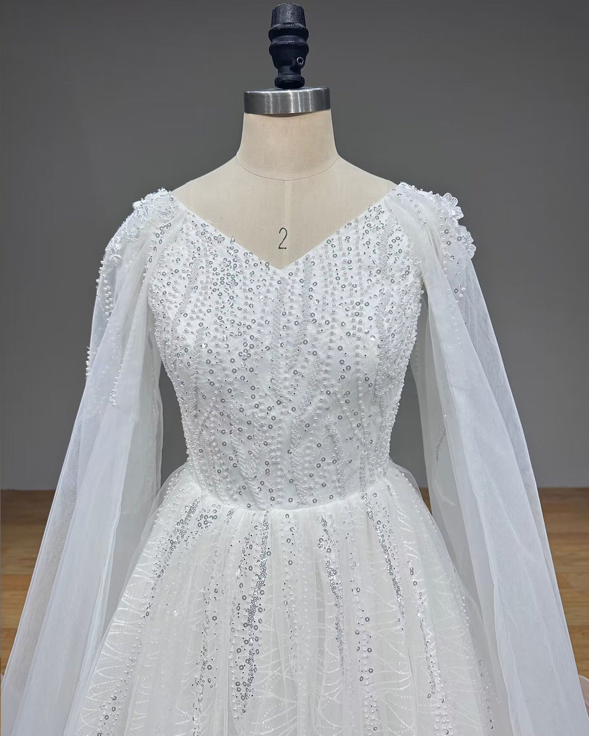 Detailed front view of a bridal gown bodice encrusted with dense pearls and sequins below a classic V-neckline.