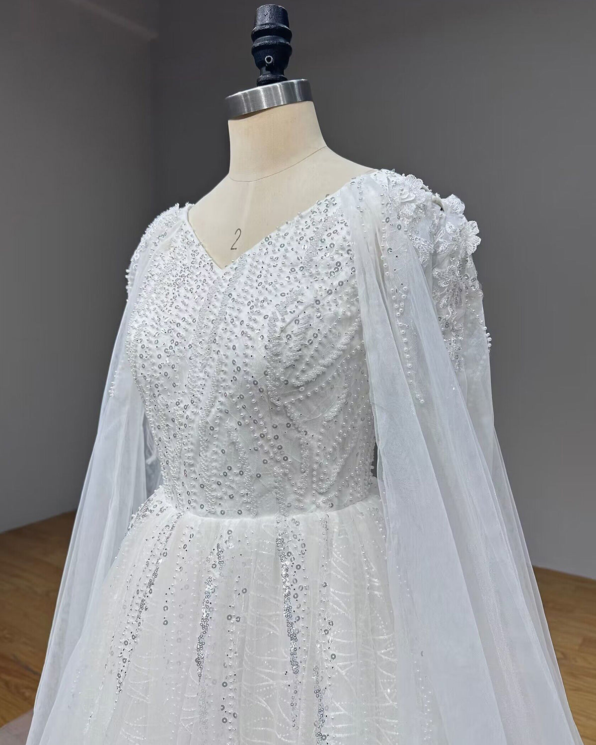 Three-quarter close-up of a modern wedding dress bodice showcasing intricate pearl beadwork and sheer cape attachments.