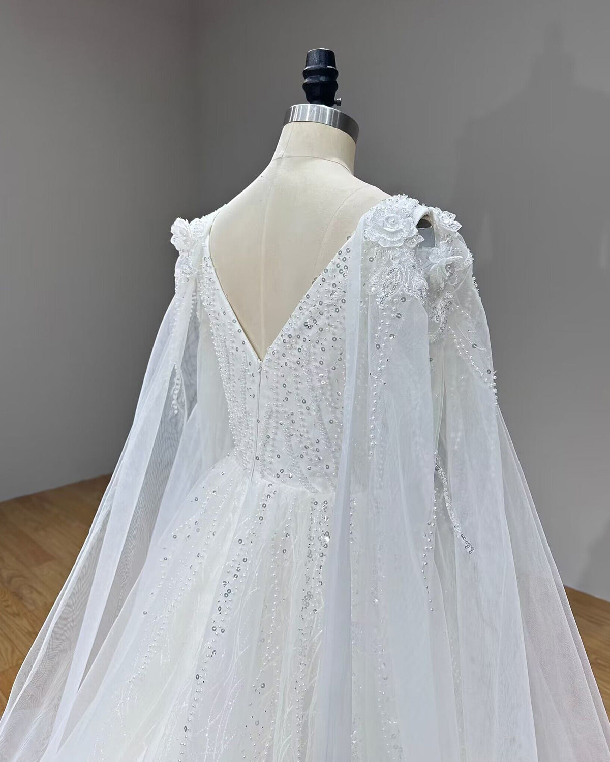 Close-up angled back view of a bridal gown highlighting the lace zipper back and dimensional floral shoulder details.