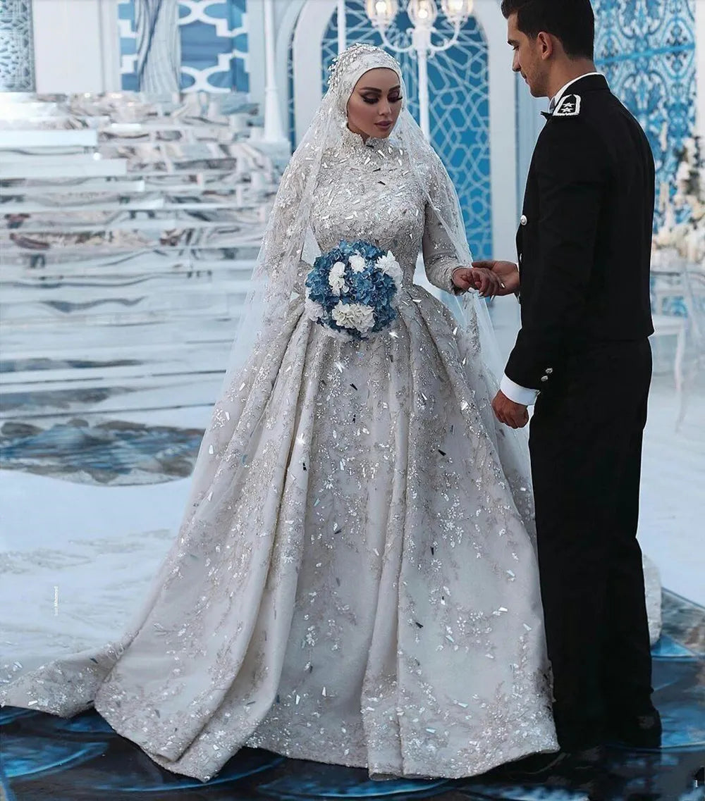 A bride and groom holding hands, showcasing the intricate lace and detailed embellishments of the Dubai-style long-sleeve wedding gown.