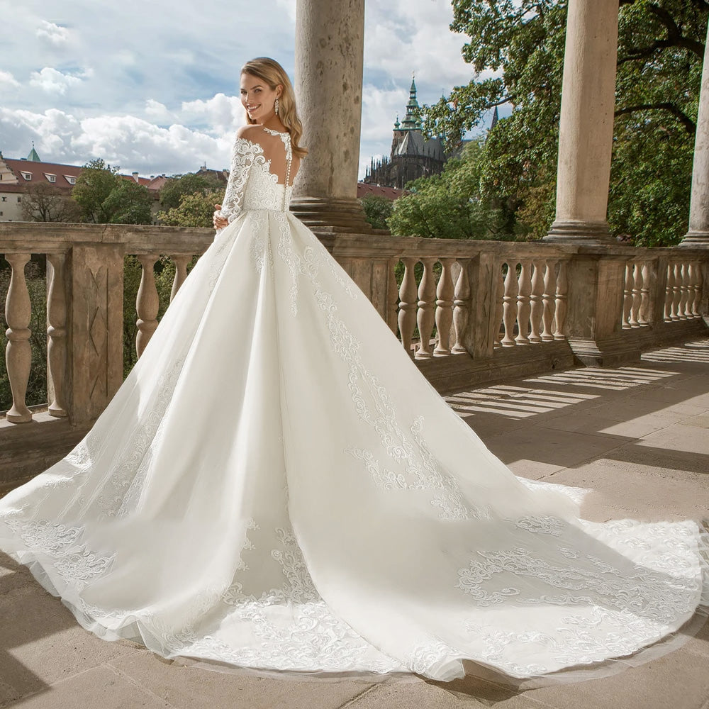 Back view of a luxurious bridal gown with an illusion lace back, long sleeves, and a flowing court train.