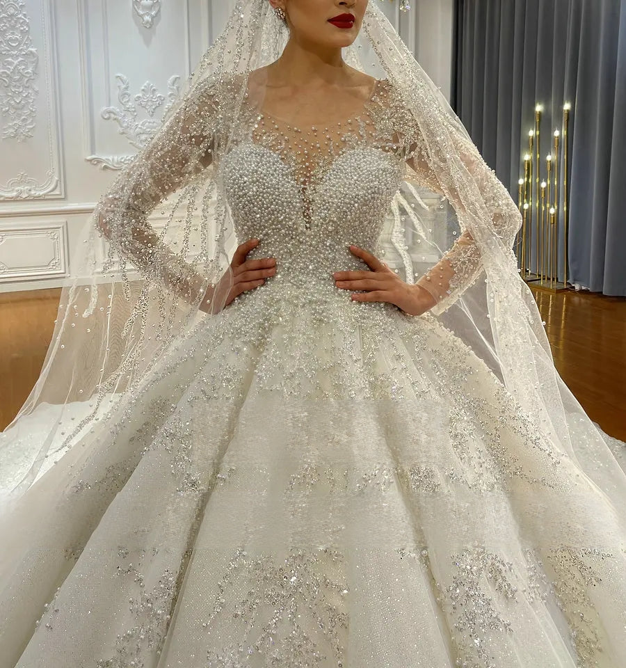 Close-up detail of a beaded wedding dress bodice, showcasing the sophisticated hand-sewn pearl and crystal embellishments on a sheer illusion neckline and sleeves.