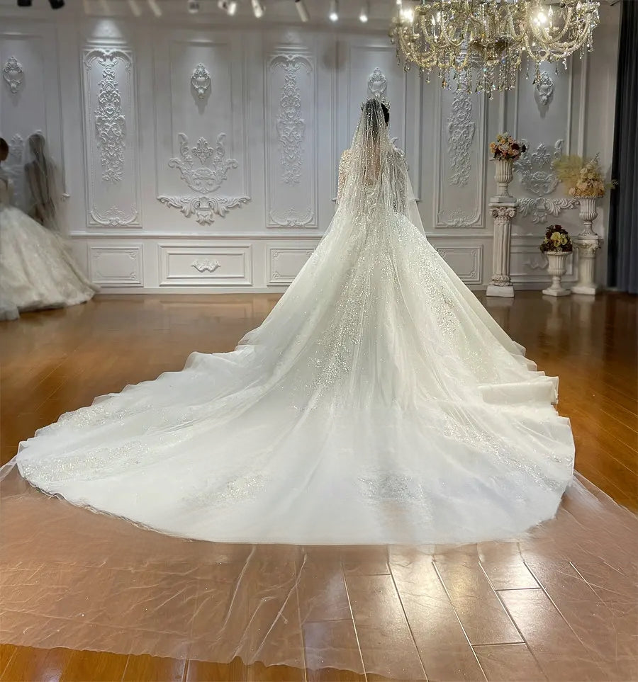 Rear perspective of a luxury wedding dress emphasizing the grand scale of the sparkling cathedral train and a matching floor-length sheer bridal veil with pearl accents.