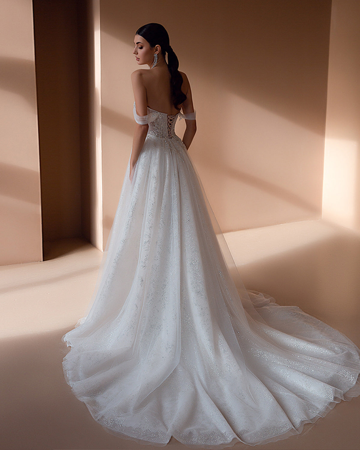 Studio back view of an A-line wedding dress on a mannequin, highlighting the deep V-back cut, traditional lace-up ribbon corset closure, and a sweeping chapel train.