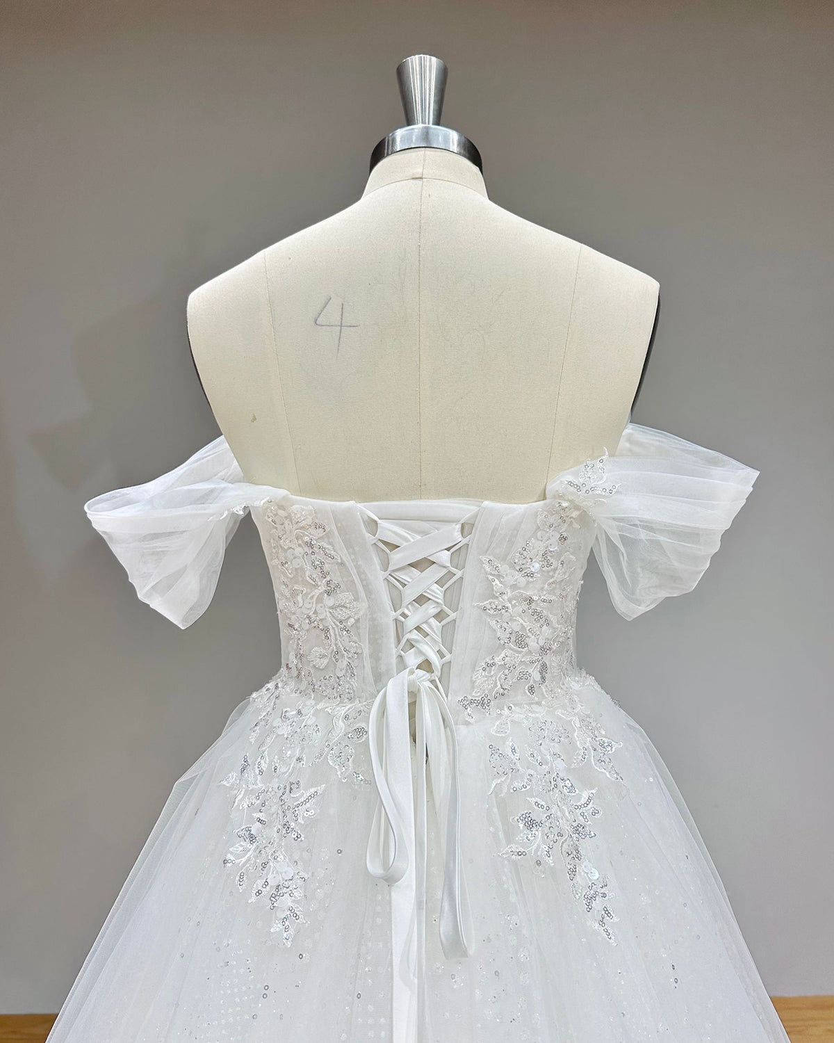 Detailed back perspective of a lace-up corset wedding dress on a dress form, emphasizing the satin ribbon ties and glittering silver floral embroidery framing the low back.
