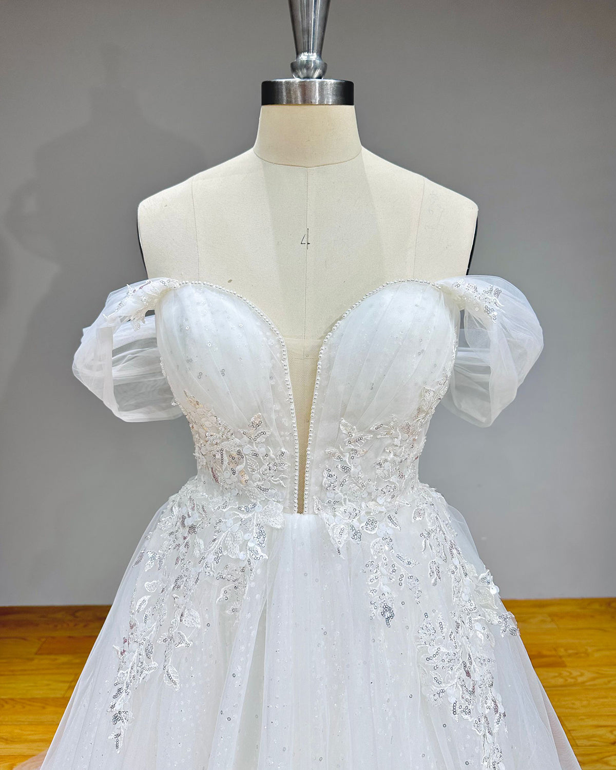 Close-up detail of a bridal bodice highlighting dense vertical rows of crystals, silver sequins, and seed pearls beneath a pleated mesh sweetheart neckline overlay.