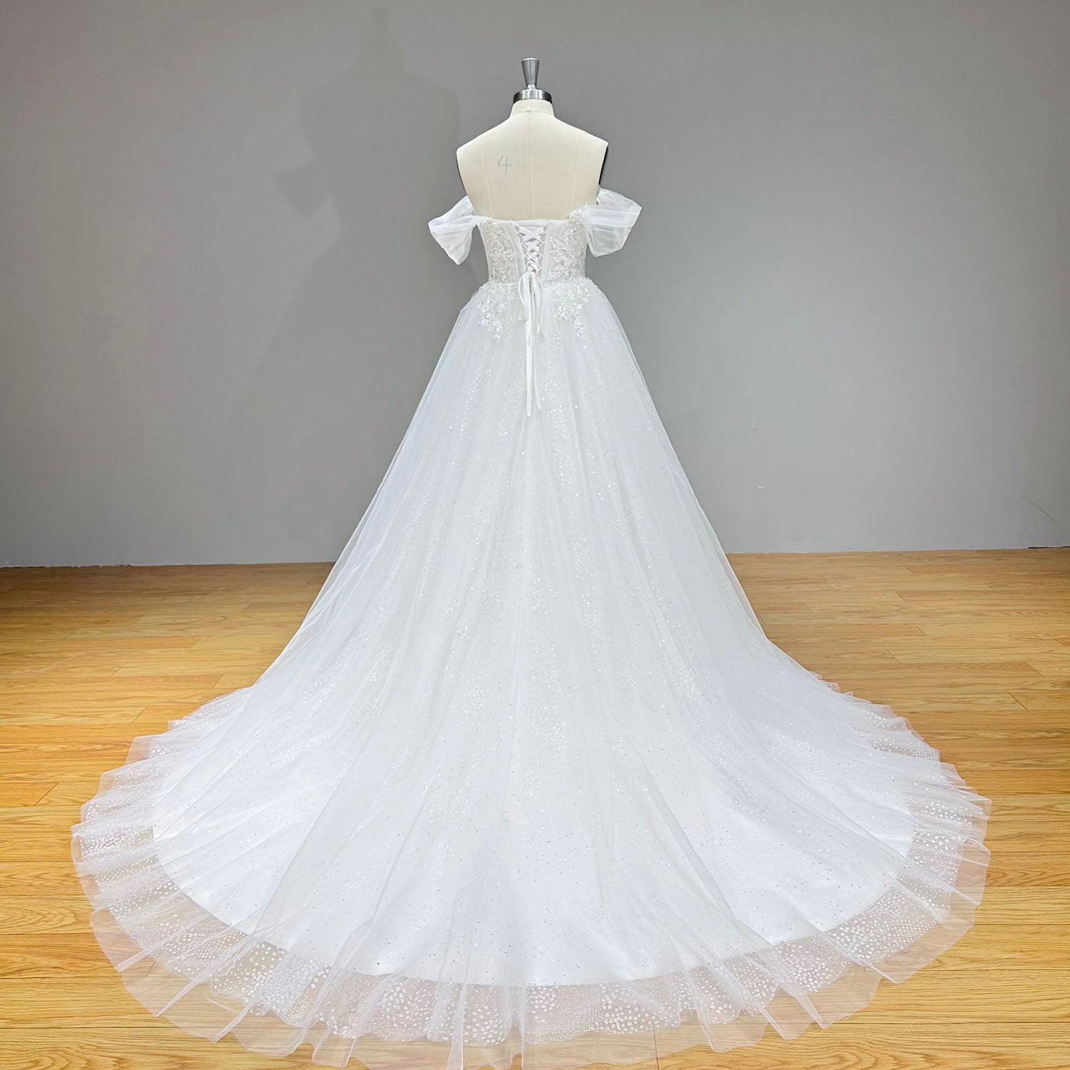 Studio back view of an A-line wedding dress on a mannequin, highlighting the deep V-back cut, traditional lace-up ribbon corset closure, and a sweeping chapel train.