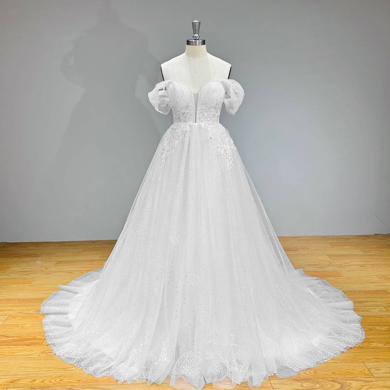 Full-length front perspective of the heavy tailored white tulle and crystal bridal dress on a mannequin against a solid gray backdrop, showing its classic romantic aesthetic.