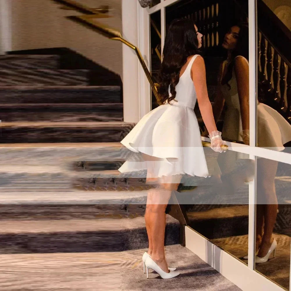 Side view of a sexy backless short satin wedding dress emphasizing the low open back cut, dainty spaghetti straps, and a structured skater-style flared mini skirt.