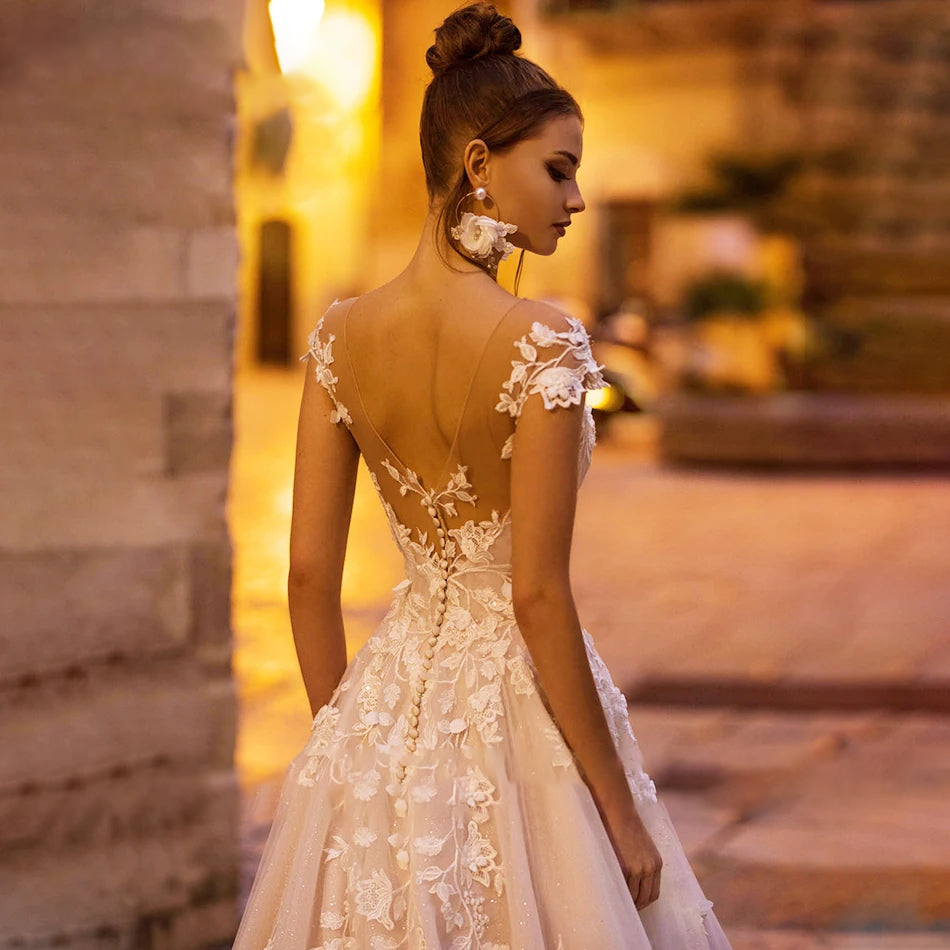 Close-up detail of the backless wedding dress bodice, highlighting the fine button closure and elaborate beaded lace appliques on sheer fabric.