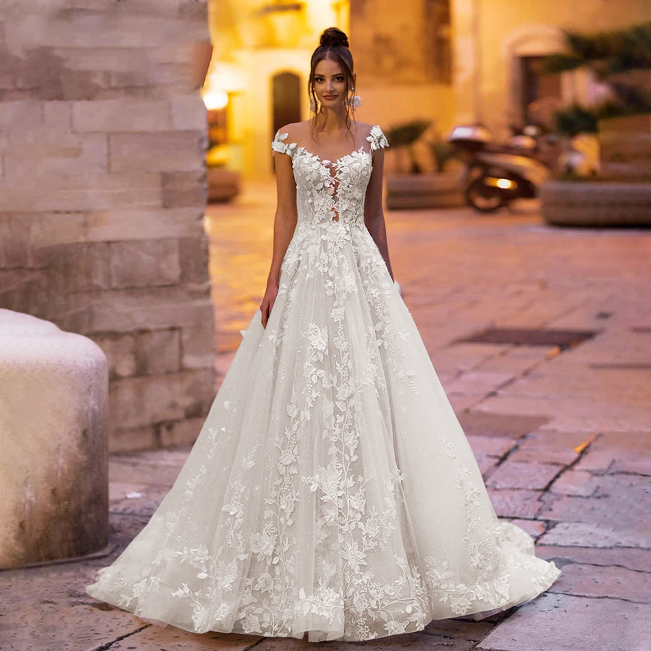 Front-facing portrait of a bride wearing a luxurious, beaded lace A-line princess gown with a graceful silhouette and delicate cap sleeves.