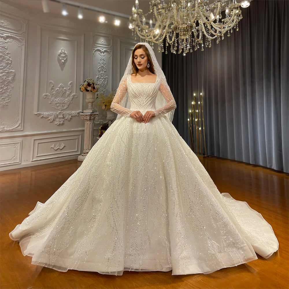 Full-length front view of an elegant A-line wedding gown featuring a square neckline, shimmering long beaded sleeves, and a voluminous sparkling skirt.