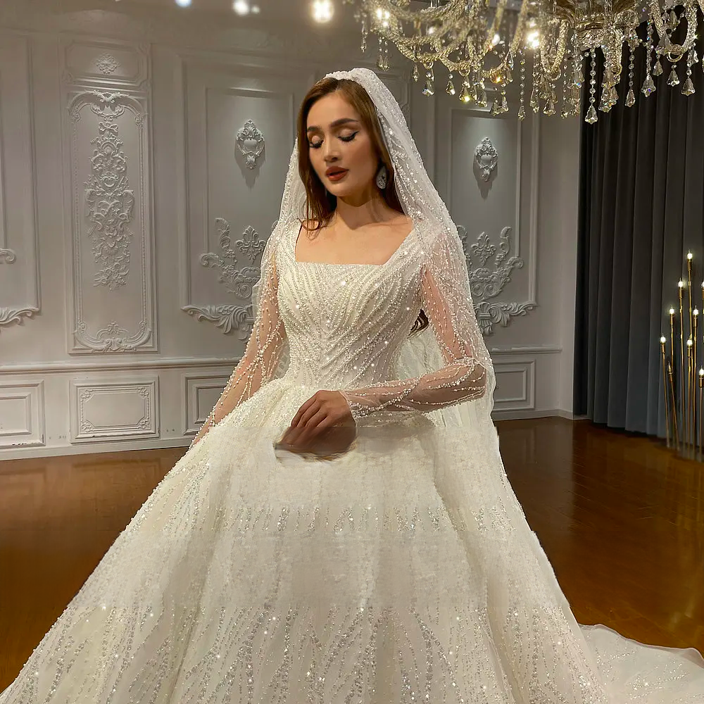 Close-up detail of a bridal gown bodice showcasing intricate chevron-patterned beadwork, a square neck, and sheer sleeves with sequin embroidery.