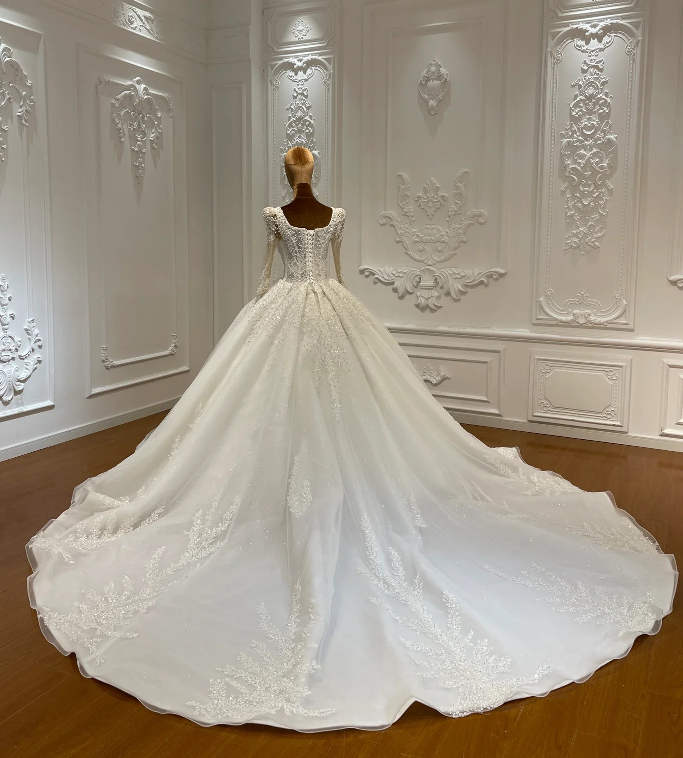 Back view of a luxury wedding gown on a mannequin, showcasing a traditional lace-up corset back and a wide, embroidered cathedral-length train.