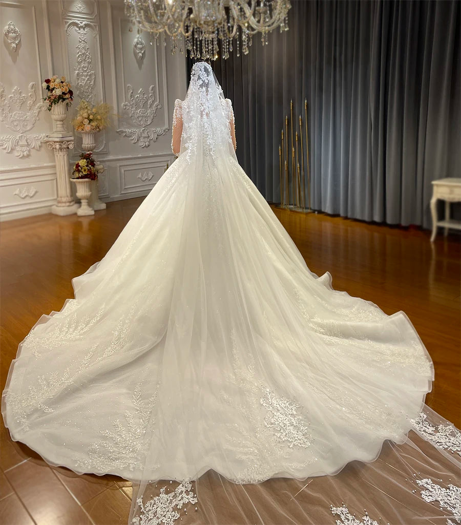 Elegant back view of a bride wearing a pearl-embellished A-line gown with a long, flowing tulle train and a matching floor-length lace veil.