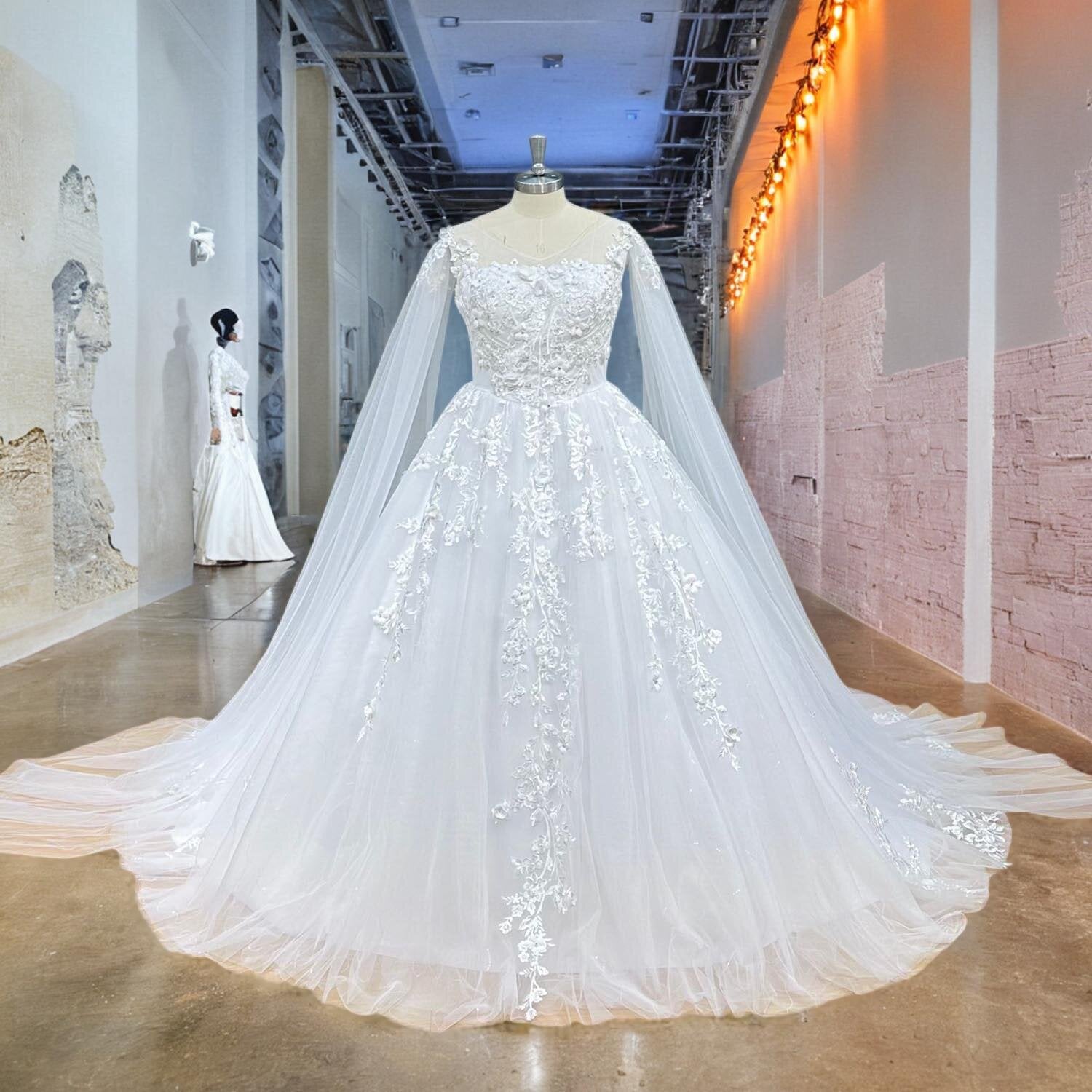 Studio front view of an elegant ball gown wedding dress on a mannequin, featuring a delicate illusion neckline, cascading vintage lace embroidery, and flowing long shawl sleeves.