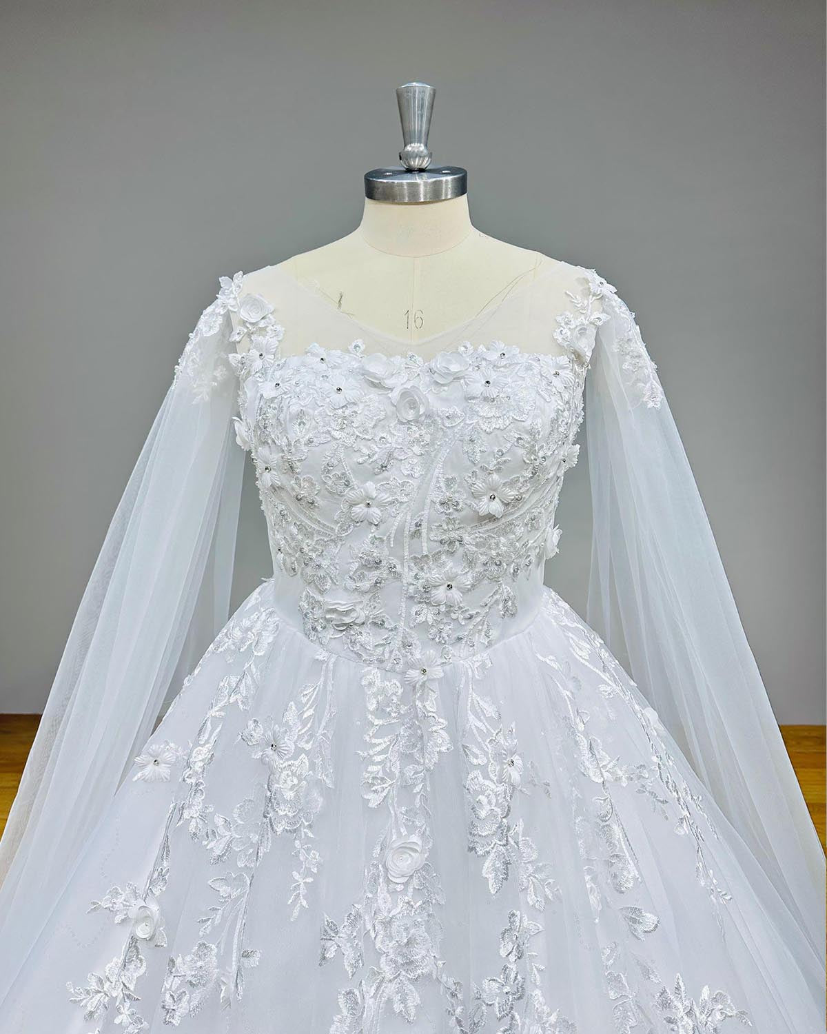 Close-up front bodice view of a vintage ball gown wedding dress, detailing the sheer illusion sweetheart neckline, intricate 3D lace floral appliques, and delicate shoulder details of the long shawl sleeves.