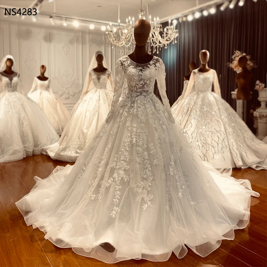 Elegant long-sleeved bridal gown on a mannequin showcasing intricate floral lace appliqués and a shimmering illusion neckline.